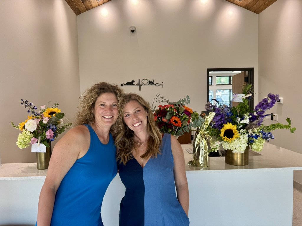 Two of the team smiling together at the front desk among opening-day flower bouquets