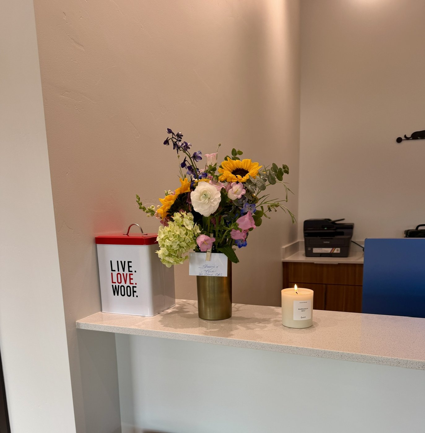 Opening-day flowers, a lit candle and a “live love woof” tin on the counter